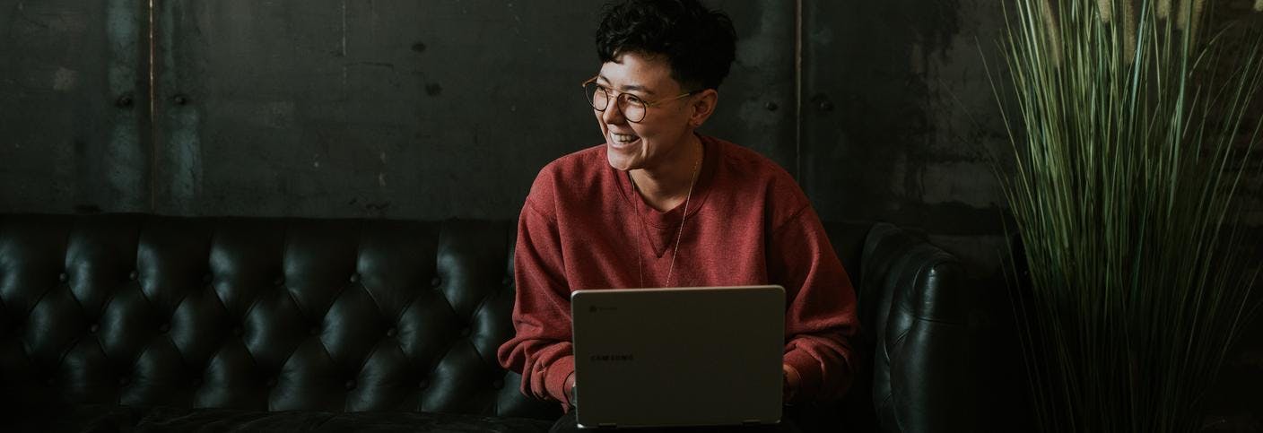 Person smiling, sat on a sofa with a laptop 